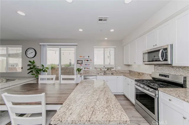 a large white kitchen with granite countertop a stove a sink a dining table and chairs