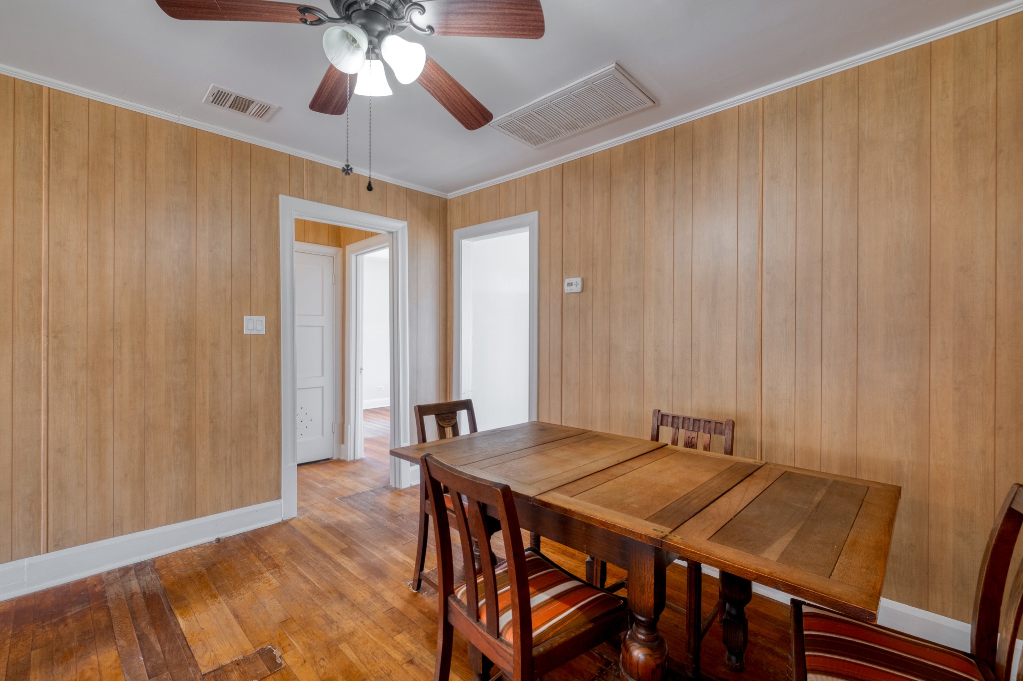 710 North Ave H Elgin, TX 78621 - Photo 10 of 25 Dining area with doorways into hallway and kitchen. Wood floors, wall paneling, and ceiling fan.