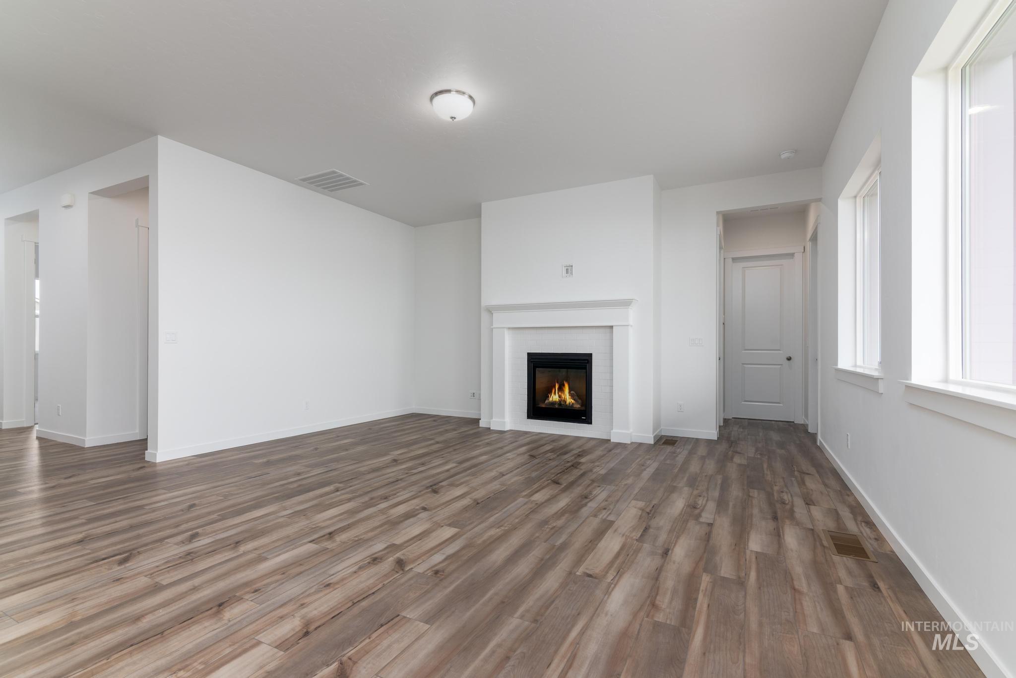 15232 Steel Cloud Avenue Caldwell, ID 83607 - Photo 5 of 33 Unfurnished living room with a warm lit fireplace and dark wood-style floors