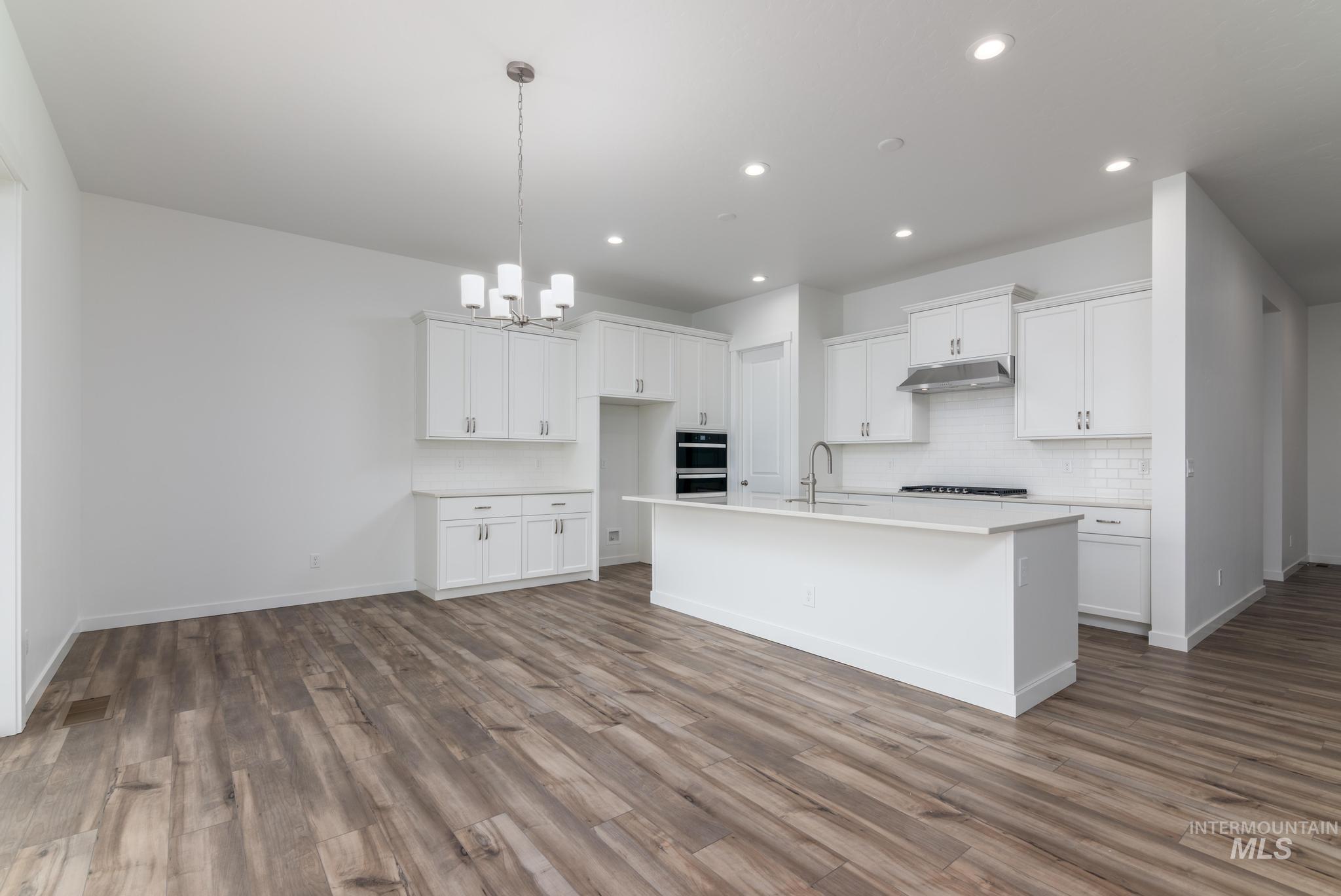 15232 Steel Cloud Avenue Caldwell, ID 83607 - Photo 8 of 33 Kitchen with white cabinetry, an island with sink, backsplash, suspended lighting, and dark wood finished floors