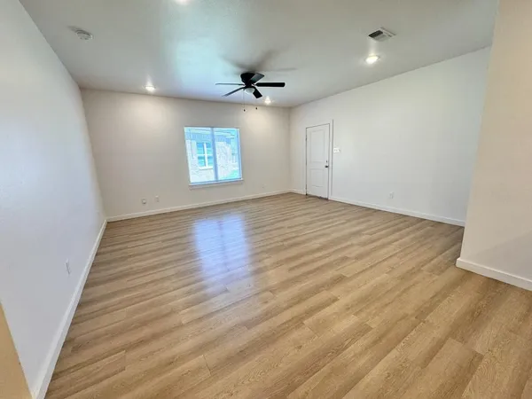 an empty room with wooden floor ceiling fan and windows