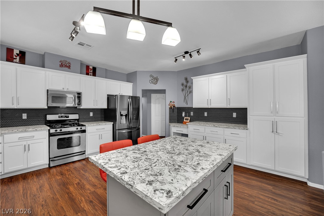 1724 Millstream Way Henderson, NV 89074 - Photo 14 of 60 A well-appointed kitchen showcasing white cabinetry, dark backsplash, and lustrous wood flooring.