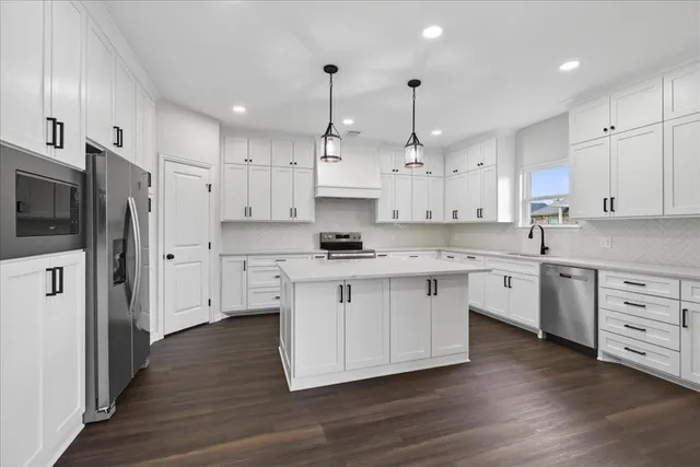 a large kitchen with stainless steel appliances granite countertop a stove a sink a refrigerator and white cabinets with wooden floor