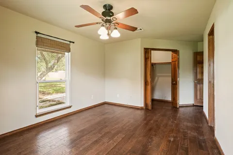 an empty room with wooden floor chandelier fan and windows