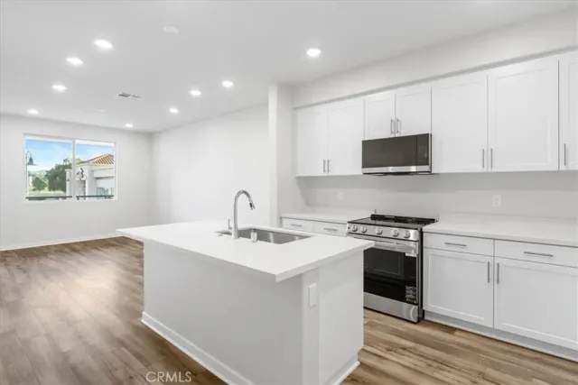 a kitchen with stainless steel appliances granite countertop a sink a stove a microwave a refrigerator with white cabinets and wooden floor