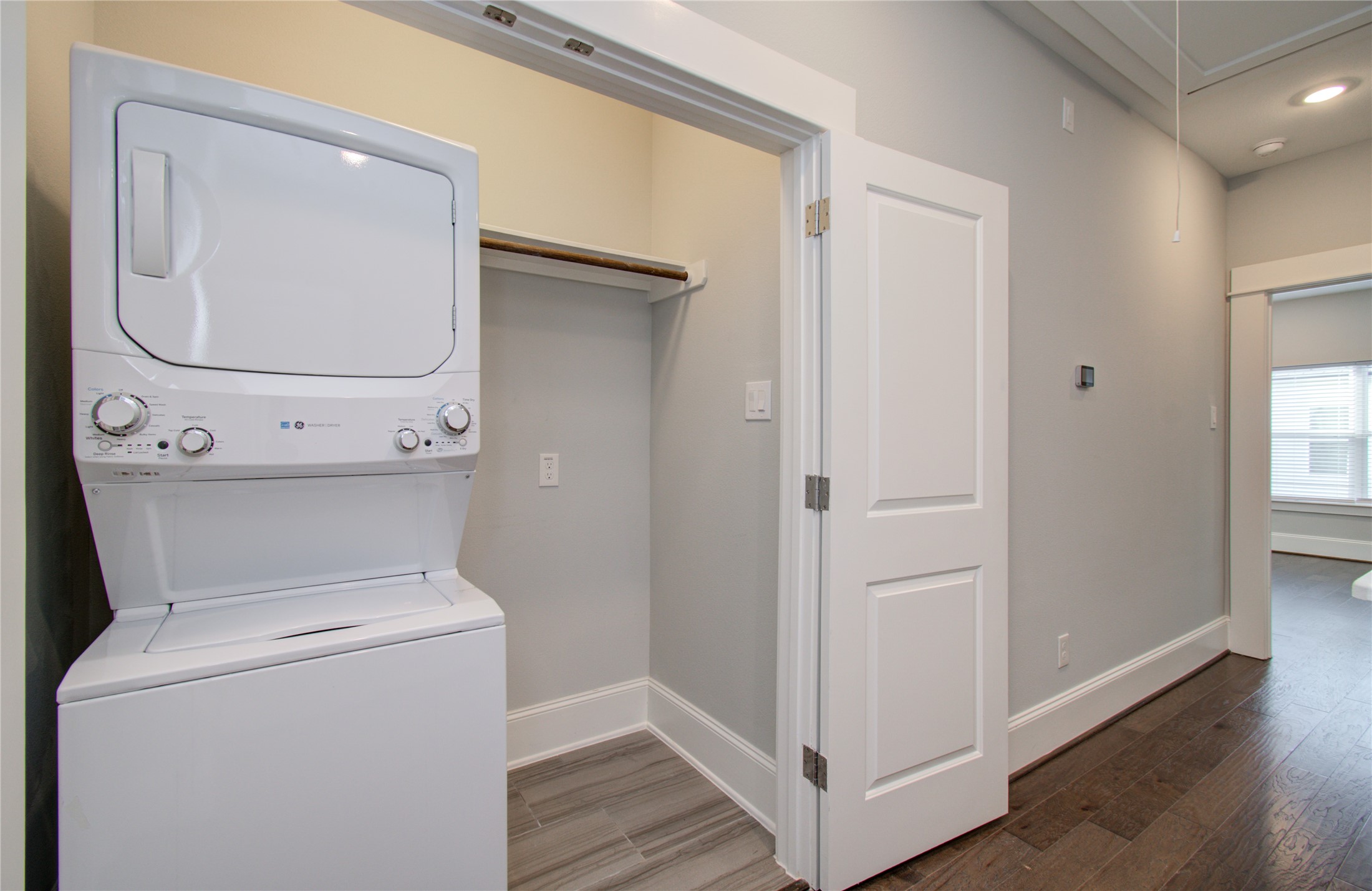 1262 North Post Oak Road, Unit A Houston, TX 77055 - Photo 30 of 50 A closer view of the laundry alcove shows the compact stacked laundry unit alongside a hanging closet rod. Neutral gray wall paint and dark hardwood floors extend through the hallway.