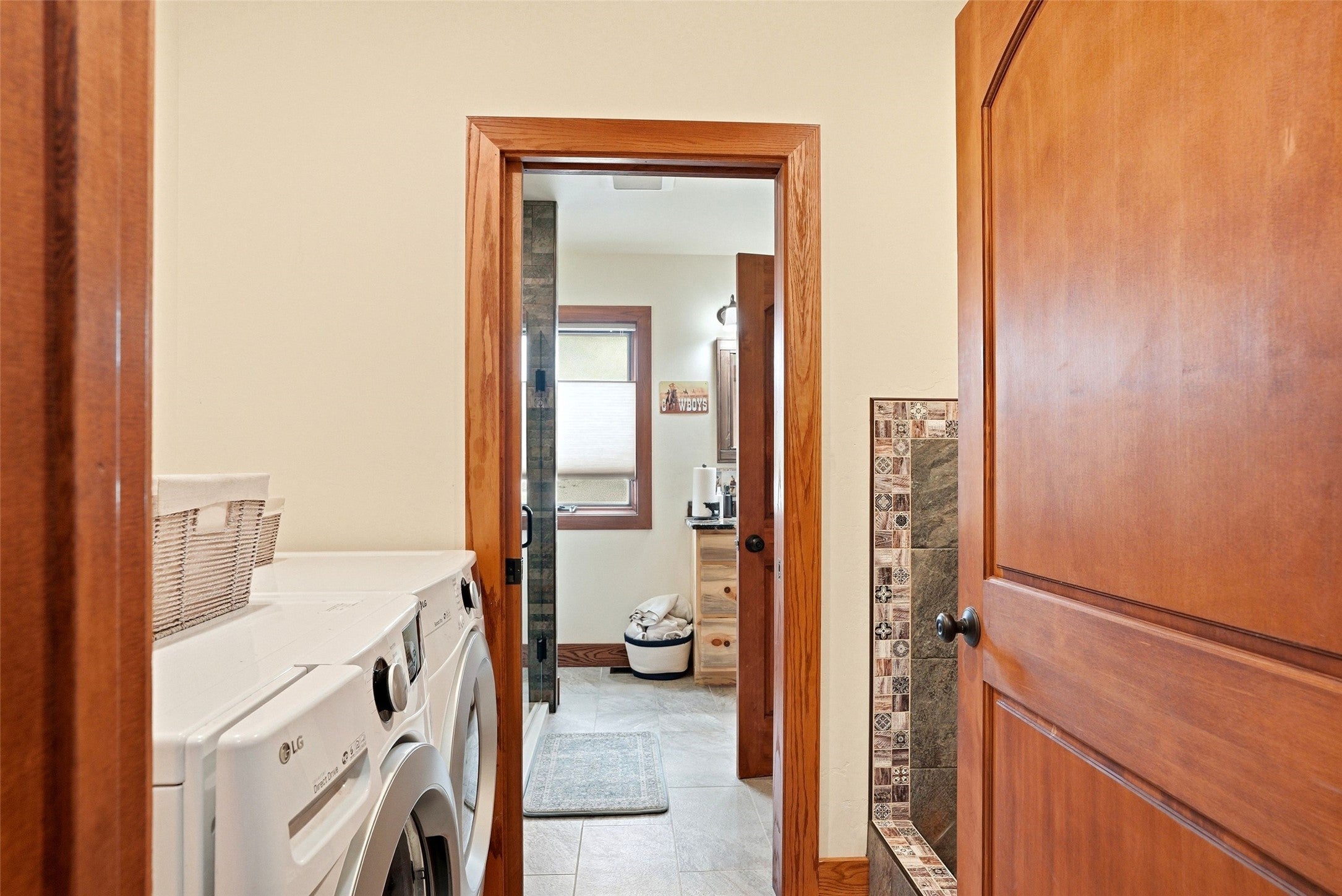 679 Hidden Valley Road North Florence, MT 59833 - Photo 37 of 85 Laundry area with a front-loading washer and dryer, featuring wood-finish door frames and a partial view into an adjacent room with tiled flooring and a vanity