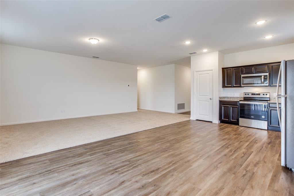 1819 Wolf Run Anna, TX 75409 - Photo 4 of 11 Open-concept living space featuring wood-finish flooring, recessed lighting, and a kitchen with dark cabinetry, stainless steel appliances, and stone countertops