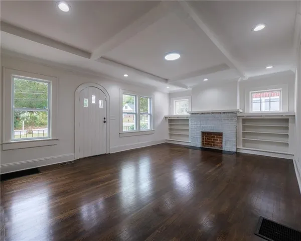 an empty room with wooden floor fireplace and windows
