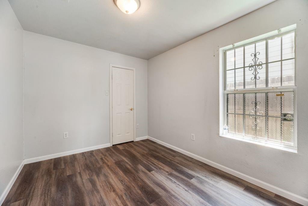 2526 Exeter Avenue Dallas, TX 75216 - Photo 17 of 19 Room featuring wood-finish flooring, light gray walls, a white paneled door, and a window with decorative security bars