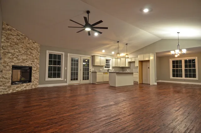 a view of an empty room with wooden floor and a kitchen
