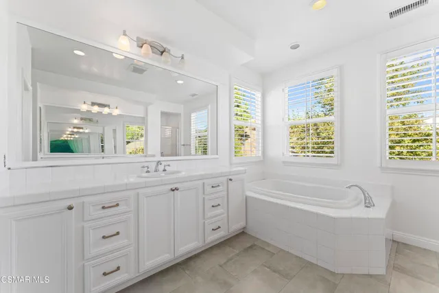 a bathroom with a granite countertop tub a double vanity sink a window and a mirror