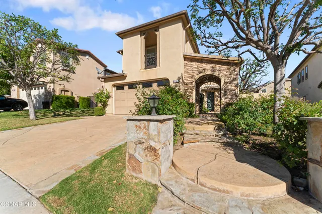 a view of a white house with a fountain plants and a large tree