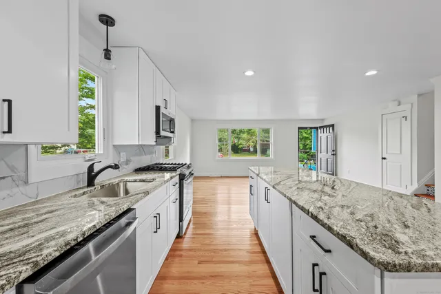 a large kitchen with granite countertop a sink and dishwasher a stove top oven with wooden floor