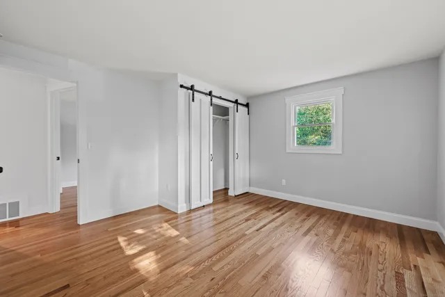 a view of an empty room with wooden floor and a window