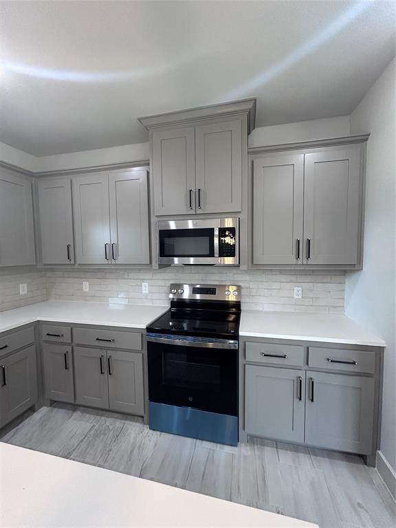 2110 Ridgewood Drive Bridgeport, TX 76426 - Photo 9 of 34 Kitchen with gray cabinetry, range, stainless steel microwave, and decorative backsplash