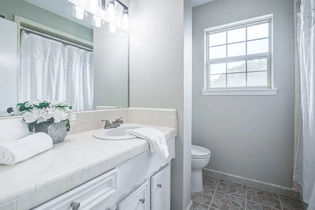 a bathroom with a granite countertop sink a toilet and a window