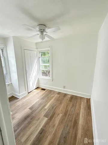 an empty room with wooden floor exposed radiator and windows