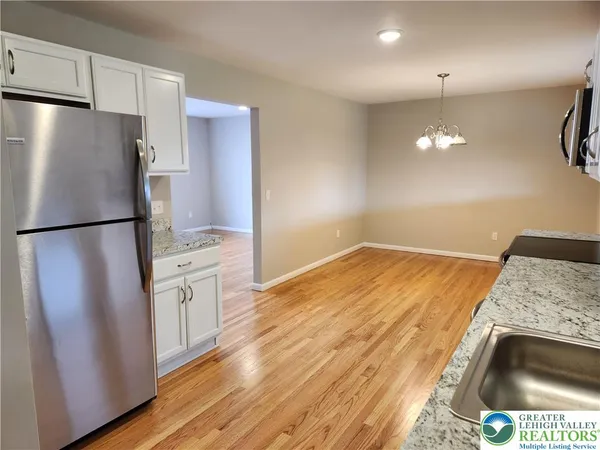 a kitchen with granite countertop a refrigerator a sink a stove and white cabinets with wooden floor