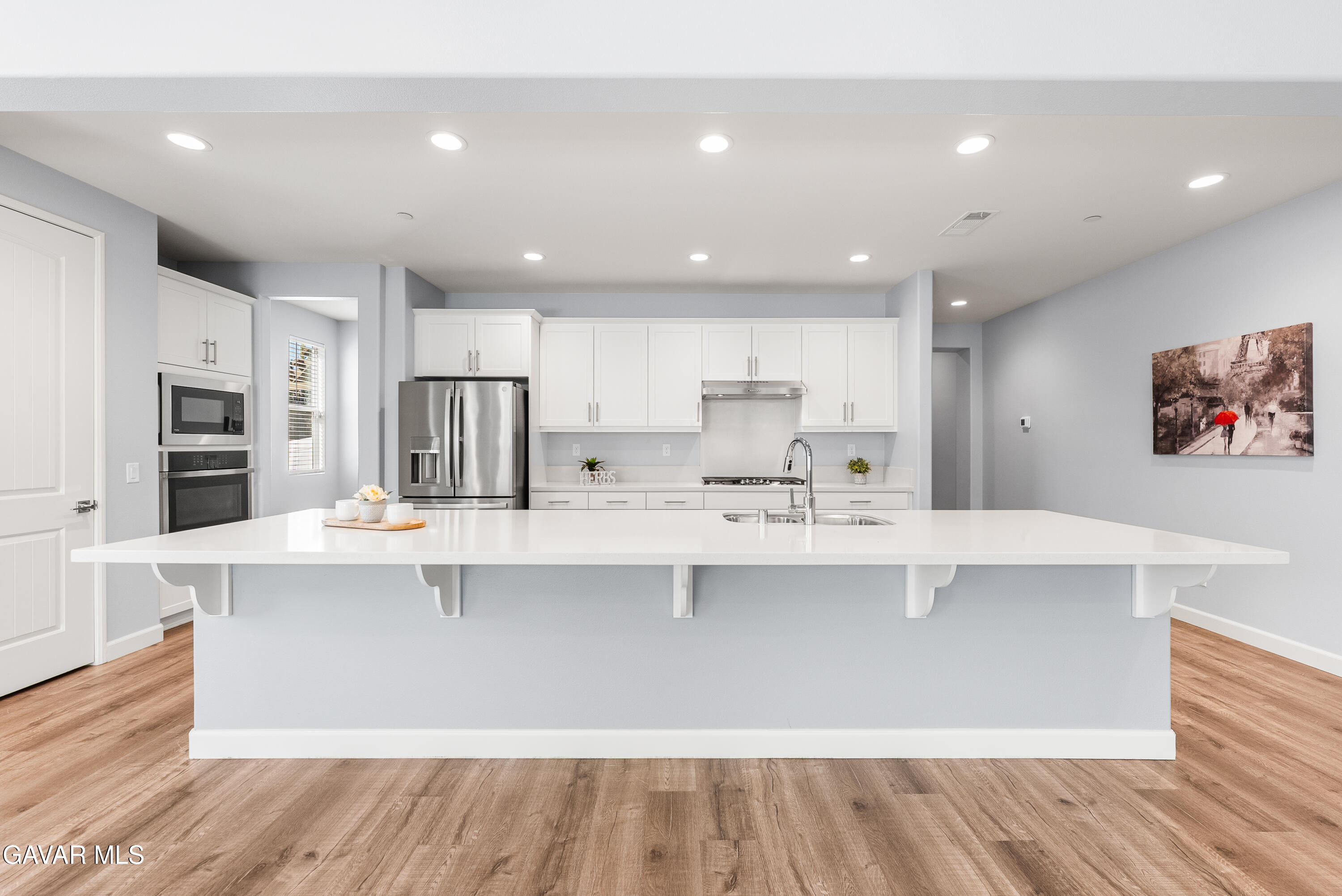 2108 Cork Oak Street Palmdale, CA 93551 - Photo 32 of 55 a large white kitchen with kitchen island a sink a stove a refrigerator and white cabinets with wooden floor