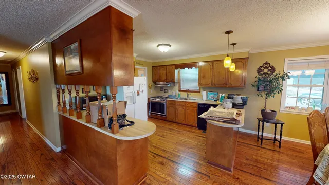 a room with stainless steel appliances kitchen island granite countertop wooden floors and a view of living room