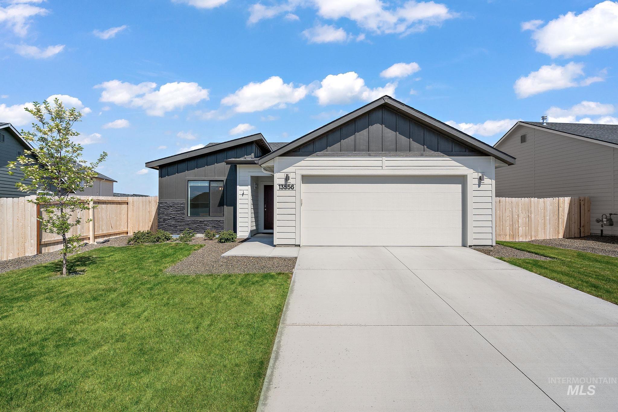 View of front of home with board and batten siding, an attached garage, driveway, and stone siding