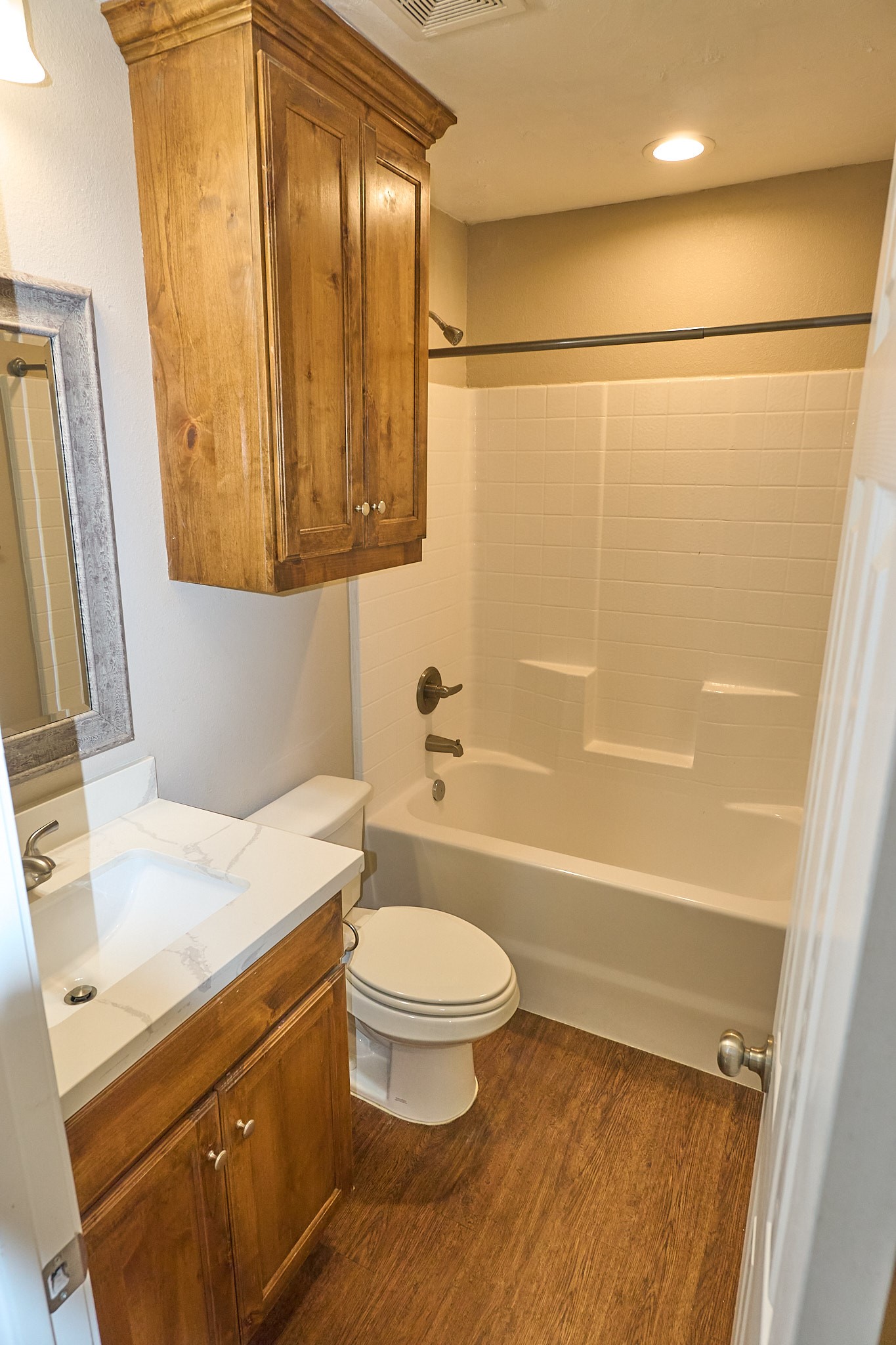 1807 Nuches Lane Bryan, TX 77803 - Photo 19 of 27 This bathroom features a clean, modern design with a white bathtub and tiled shower, wooden cabinets for storage, a compact sink with a white countertop, and warm wood flooring.