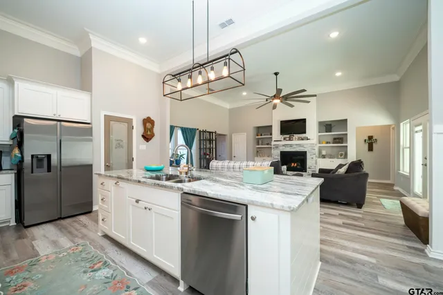 a open kitchen with stainless steel appliances granite countertop a sink dishwasher a refrigerator and a fireplace with wooden floor