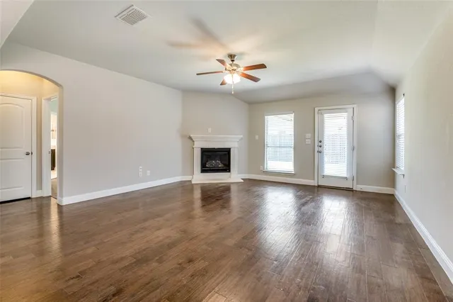 an empty room with wooden floor fan and windows
