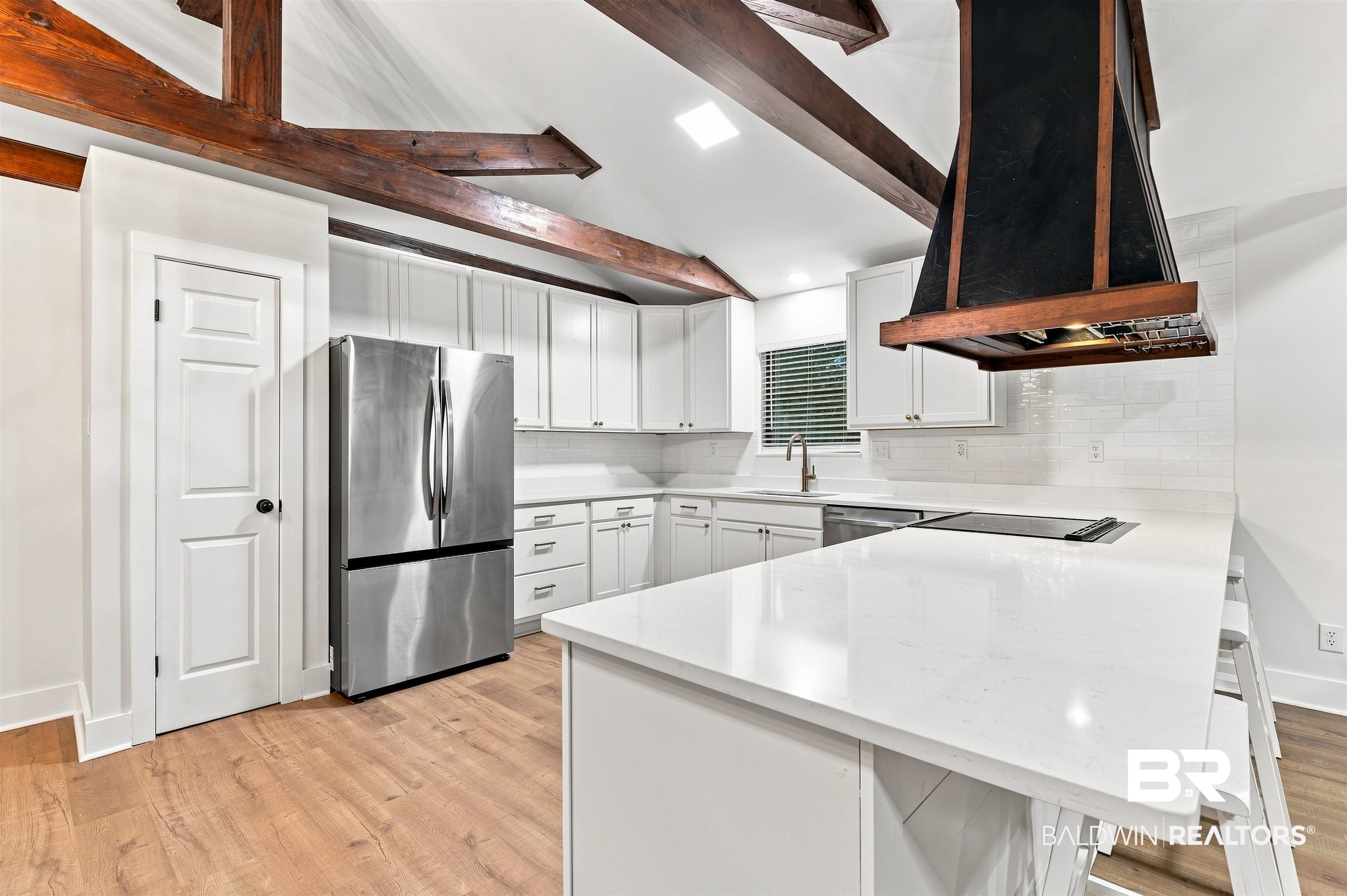599 Ridgewood Drive Daphne, AL 36526 - Photo 11 of 41 Vaulted ceiling kitchen featuring exposed wood beams, white shaker cabinetry, stainless steel appliances, a built-in cooktop, and light wood-finish flooring