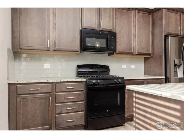 a living room with stainless steel appliances granite countertop a refrigerator a sink dishwasher a stove and a dining table with wooden floor