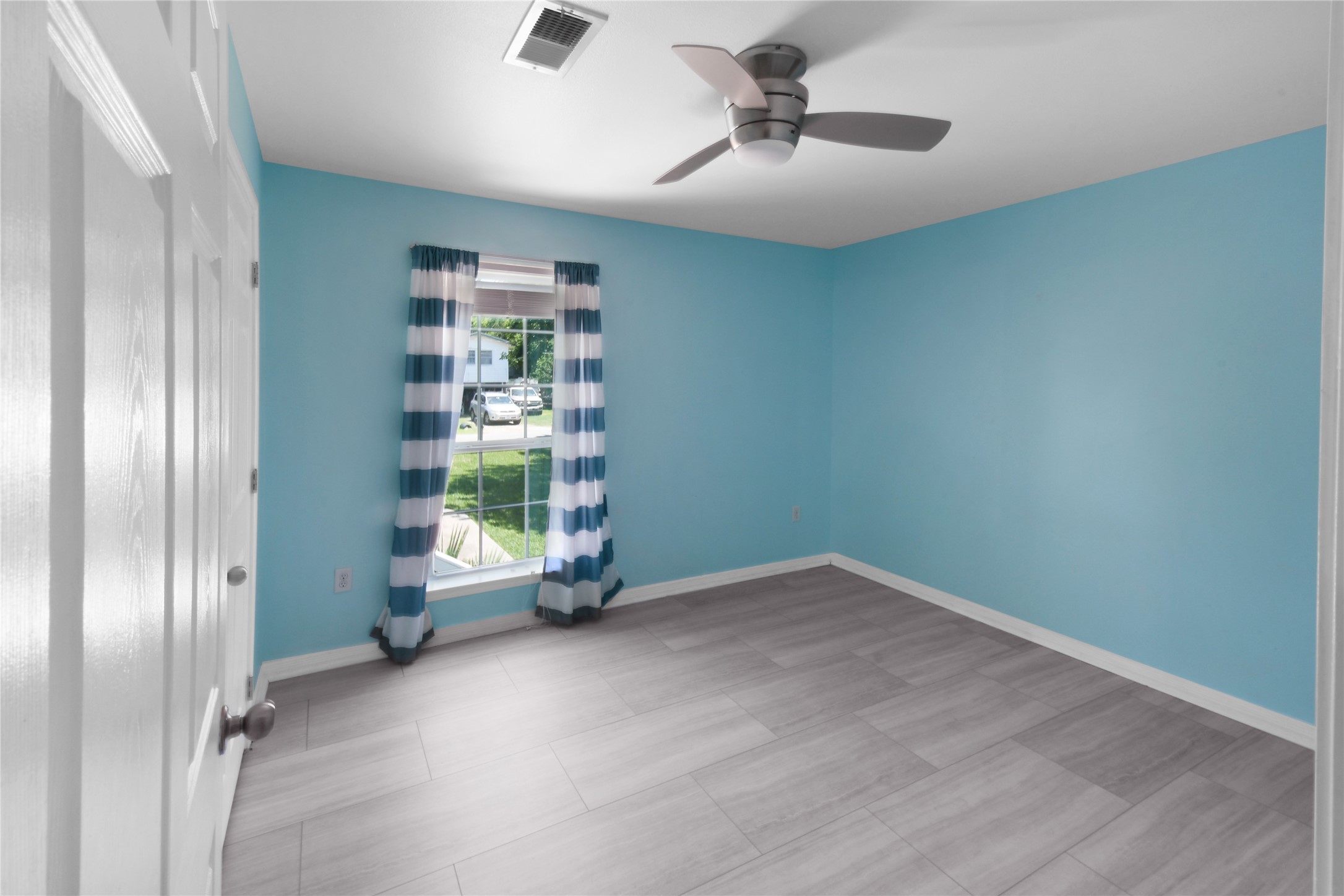 320 10th Street Dickinson, TX 77539 - Photo 20 of 21 Discover a serene retreat in Bedroom 2, featuring soft blue walls, modern tile flooring, and abundant natural light through a large window, perfect for relaxation and comfort.