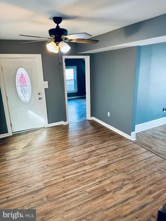 a view of an empty room with wooden floor and a ceiling fan