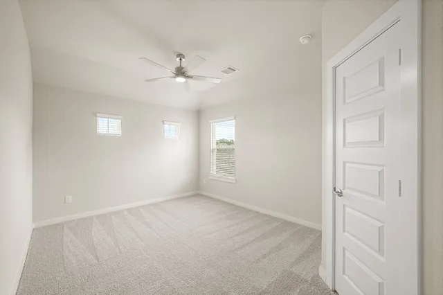 an empty room with chandelier fan and windows