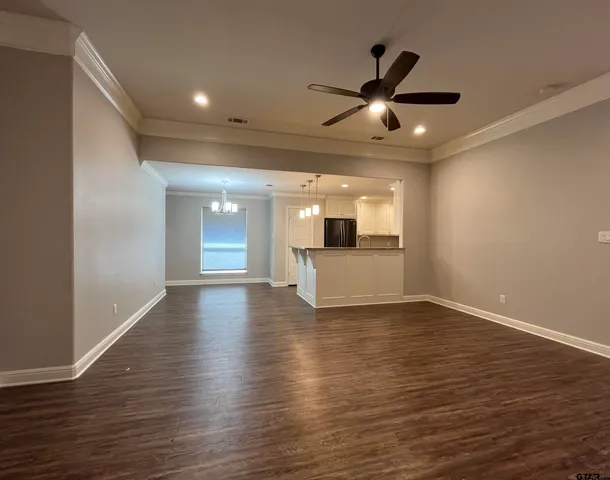 a view of an empty room with wooden floor and a ceiling fan