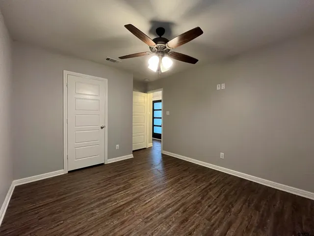 a view of an empty room with wooden floor and a ceiling fan
