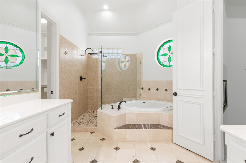 967 East Bethel School Road Coppell, TX 75019 - Photo 27 of 39 Spacious bathroom featuring a built-in jetted tub, a glass-enclosed shower with pebble flooring, and dual vanity areas with white cabinetry and solid surface countertops