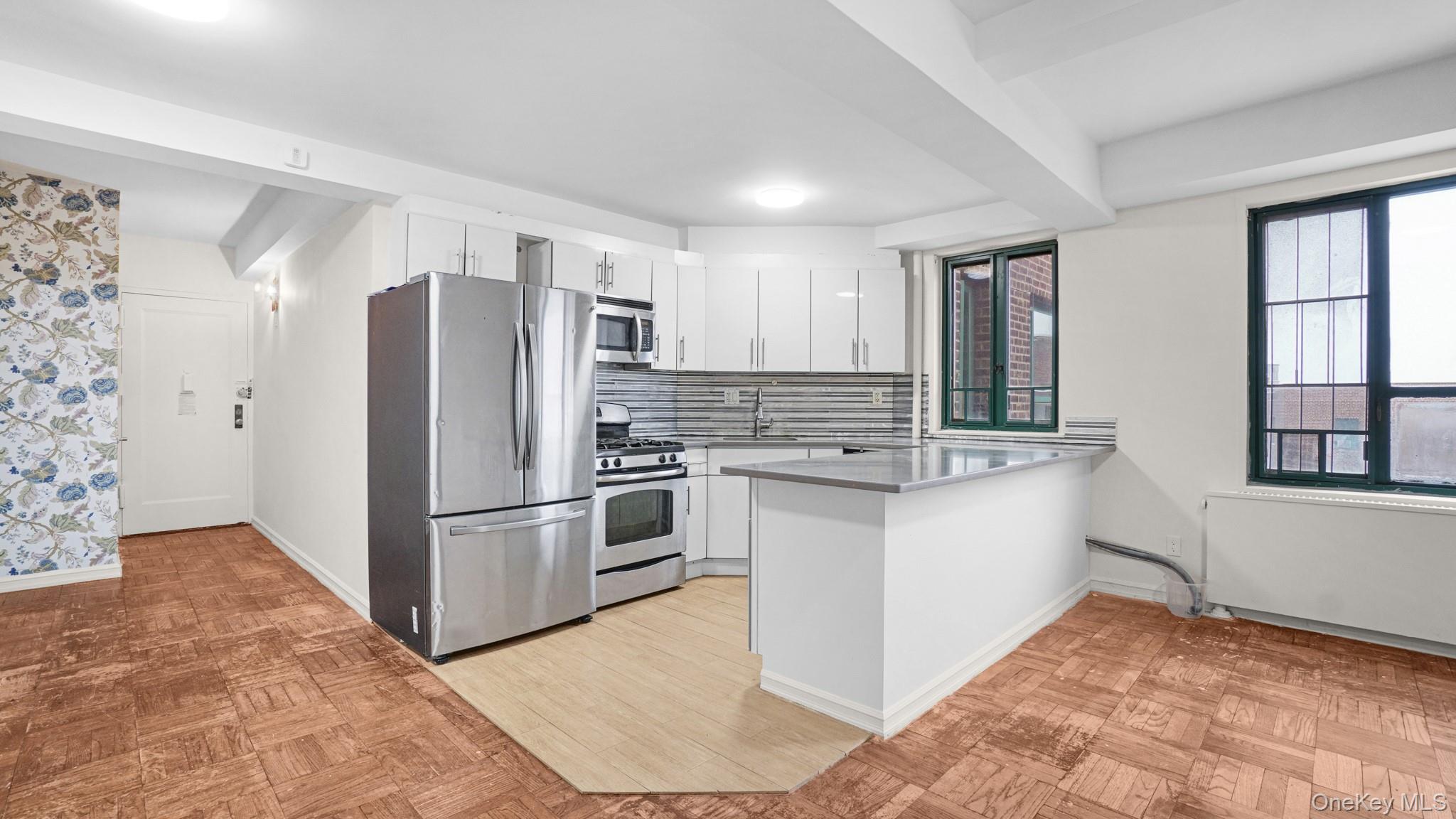 2220 East Tremont Avenue, Unit 7F Bronx, NY 10462 - Photo 4 of 13 Kitchen with appliances with stainless steel finishes, white cabinets, a peninsula, tasteful backsplash, and light countertops