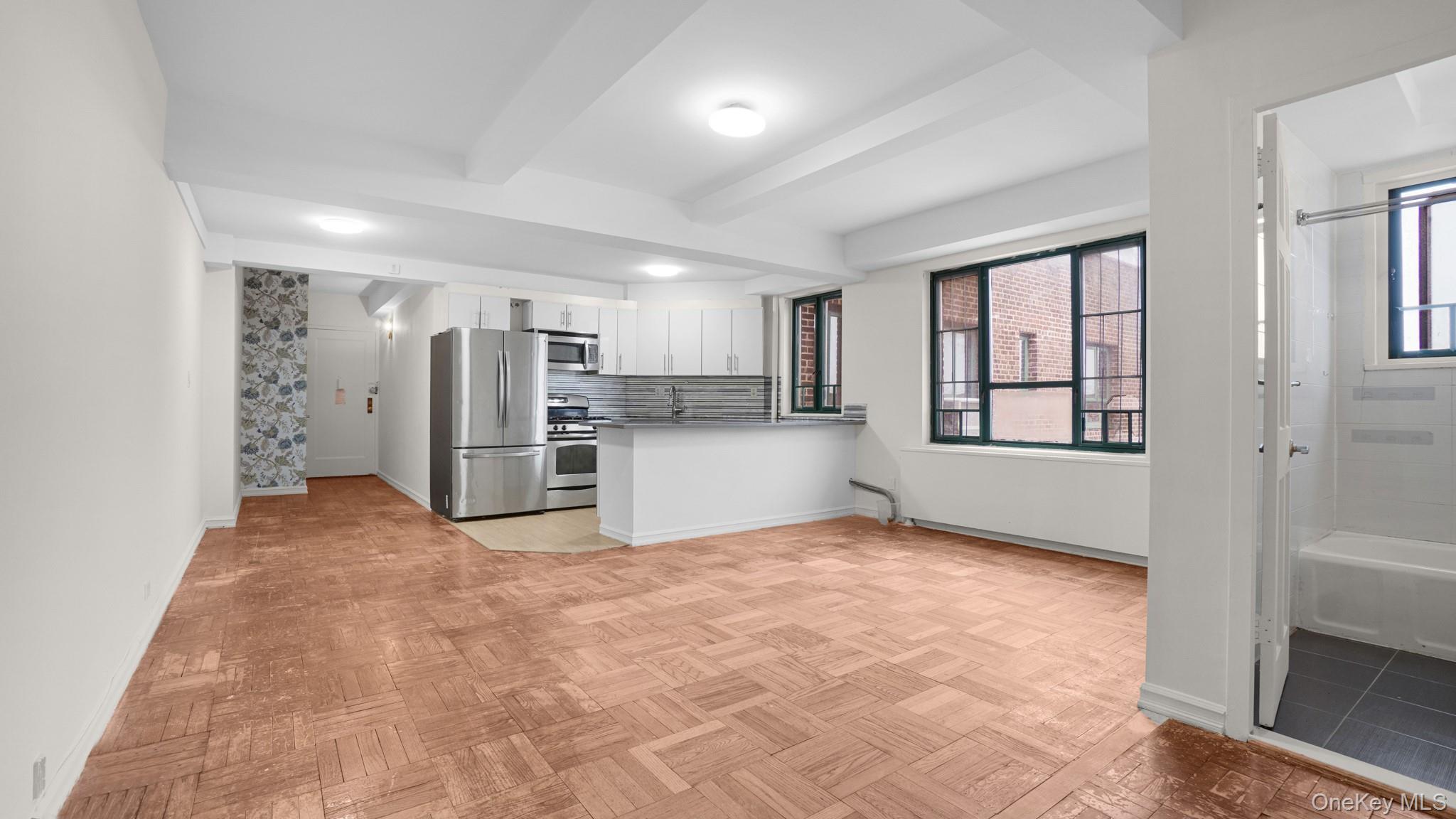 2220 East Tremont Avenue, Unit 7F Bronx, NY 10462 - Photo 5 of 13 Kitchen featuring stainless steel appliances, tasteful backsplash, a peninsula, white cabinets, and beam ceiling
