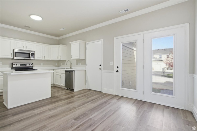 4496 West 11800 South South Jordan, UT 84009 - Photo 11 of 33 Kitchen with light countertops, white cabinetry, stainless steel appliances, crown molding, and light wood-style floors