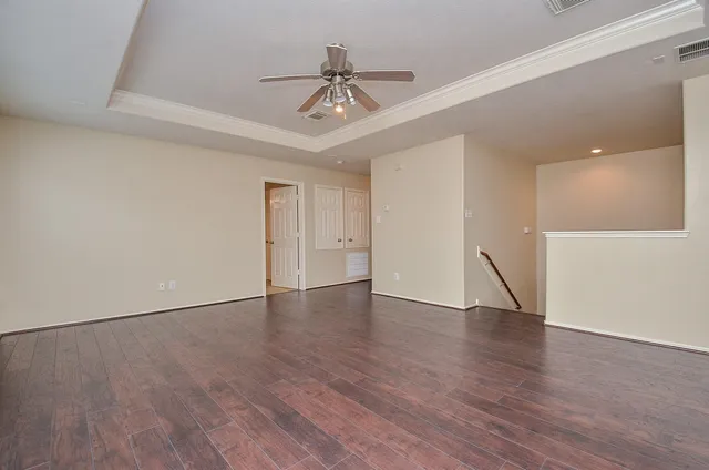 a view of an empty room with wooden floor and a ceiling fan