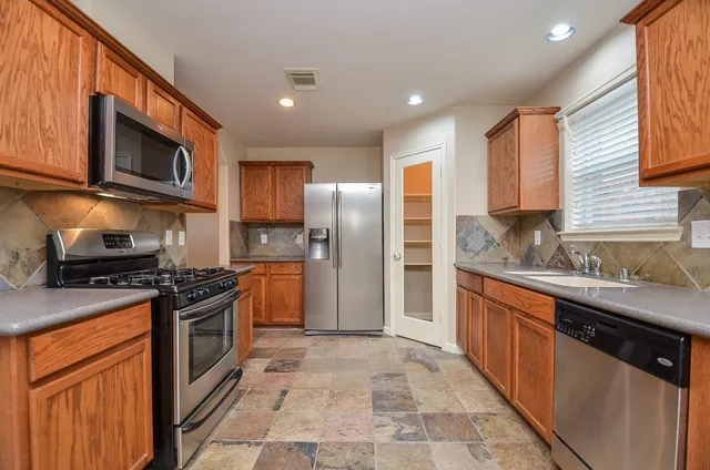 a kitchen with stainless steel appliances granite countertop a stove top oven a sink dishwasher a refrigerator and cabinets with wooden floor