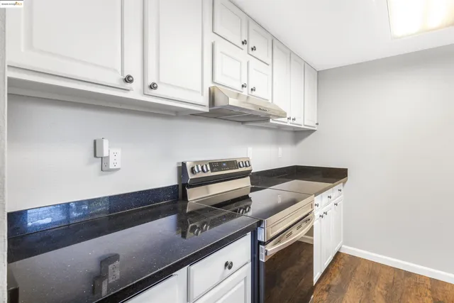 a kitchen with granite countertop a stove and a white cabinets