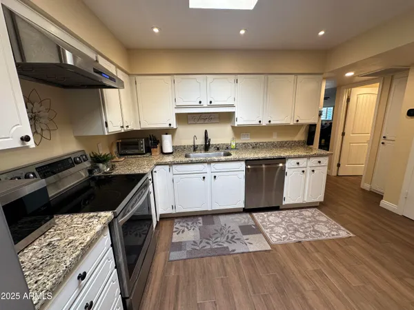 a kitchen with stainless steel appliances granite countertop a refrigerator oven a sink dishwasher a dining table and chairs with wooden floor