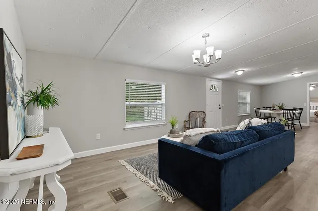 a living room with furniture a chandelier a large window and wooden floor