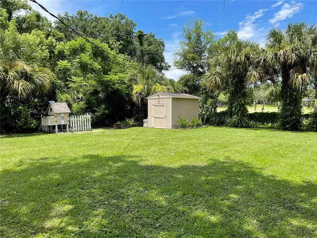 a view of a white house with a small yard and large trees