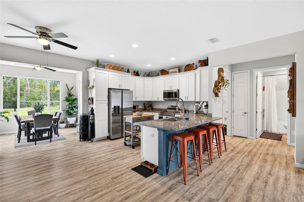 3699 Southwest 177th Lane Road Ocala, FL 34473 - Photo 3 of 26 a kitchen with stainless steel appliances a stove top oven a refrigerator a dining table and chairs with wooden floor