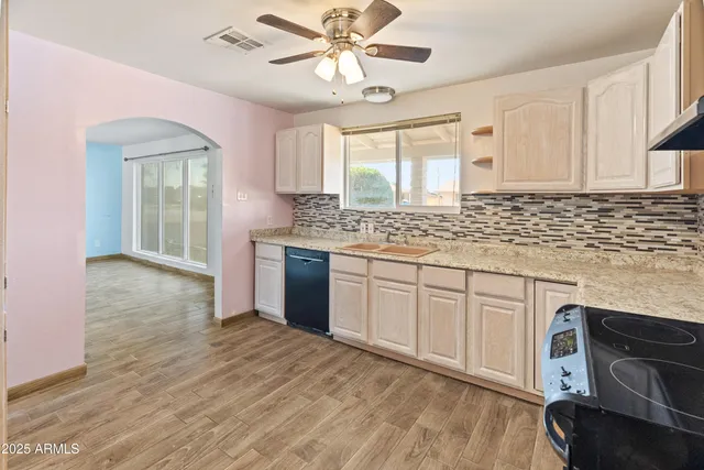 a kitchen with stainless steel appliances granite countertop a stove a sink dishwasher and white cabinets with wooden floor