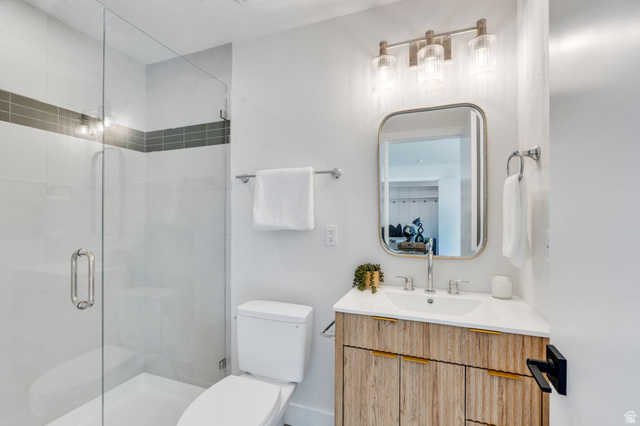 3813 North Foothill Drive Provo, UT 84604 - Photo 31 of 71 Contemporary bathroom featuring a clear glass shower enclosure, a wood-finish vanity with gold-tone hardware, a rectangular vanity mirror, and modern three-light sconce