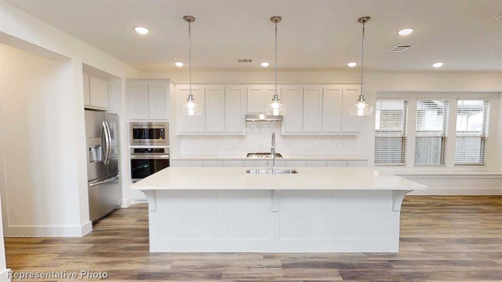 a large kitchen with kitchen island a stove a sink a refrigerator and white cabinets with wooden floor